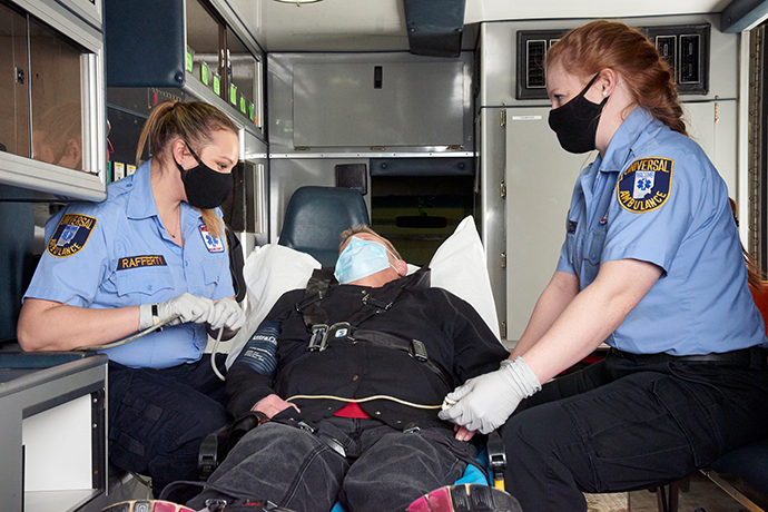 Two female first responders checking a person&#039;s vitals in the back of an ambulance