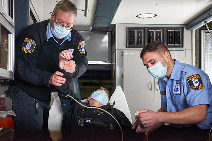 Two male first responders checking a person&#039;s vitals in the back of an ambulance