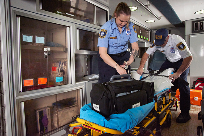 Two first responders putting away supplies in the back of an ambulance