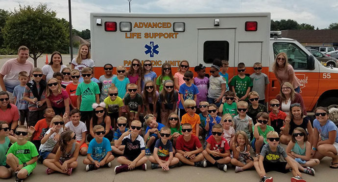 A large group of children posing in front of an ambulance for a group photo